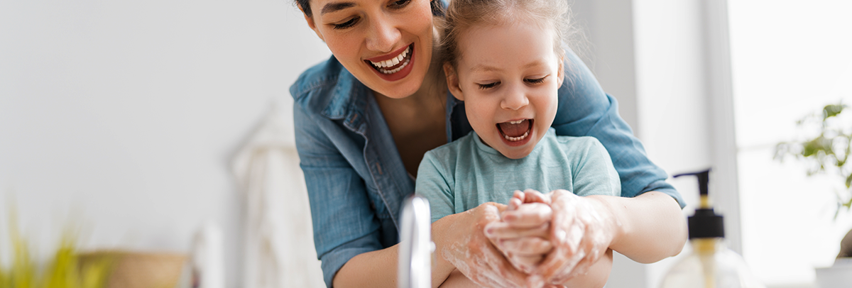 A mother and young daughter washing hands with soap in the sink together