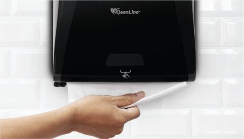 A person's hand dispensing a paper towel from KleenLine towel dispenser in the restroom
