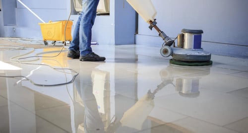 A custodian scrubbing the floor with a scrubber