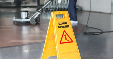 A sign says cleaning in progress over a person using floor scrubber in the background