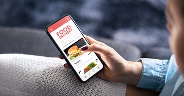 A female holding a mobile phone showing food delivery app with a picture of burger
