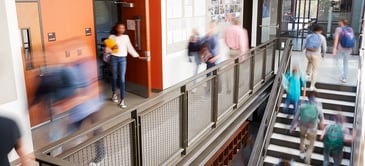 An image of school hallway with stairs with students walking around