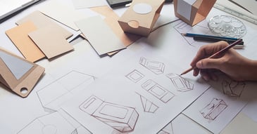 A hand of a designer working on various packaging box designs