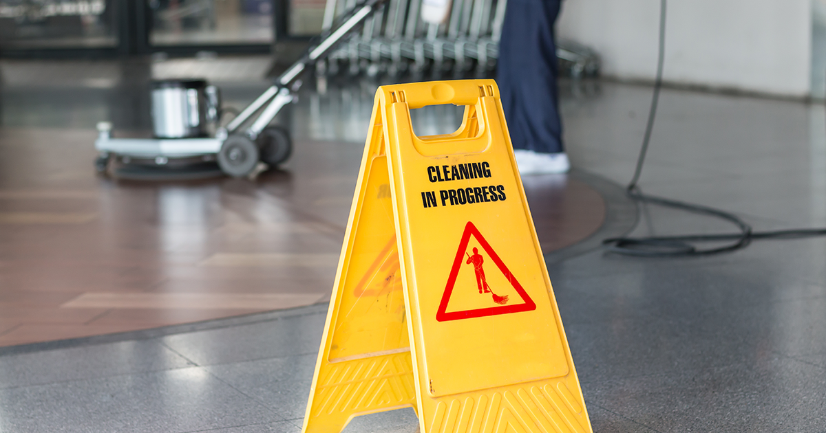 A sign says cleaning in progress with a janitor cleaning floor with a scrubber in the background.