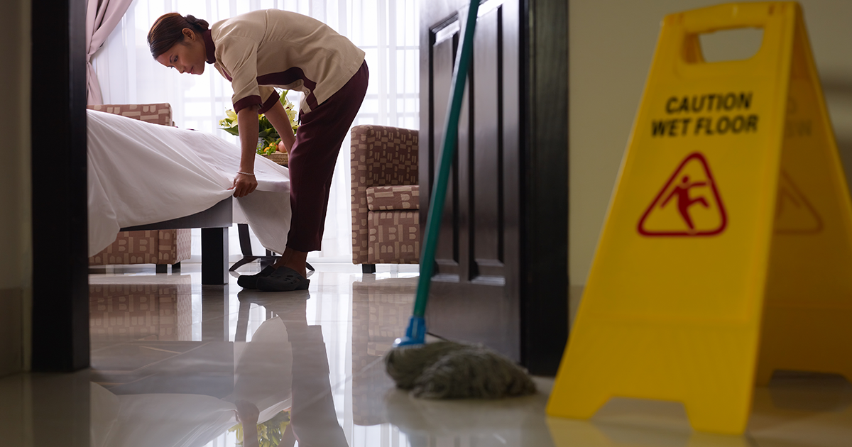 A housekeeping staff cleaning the hotel room with caution wet floor sign in front of the hotel room