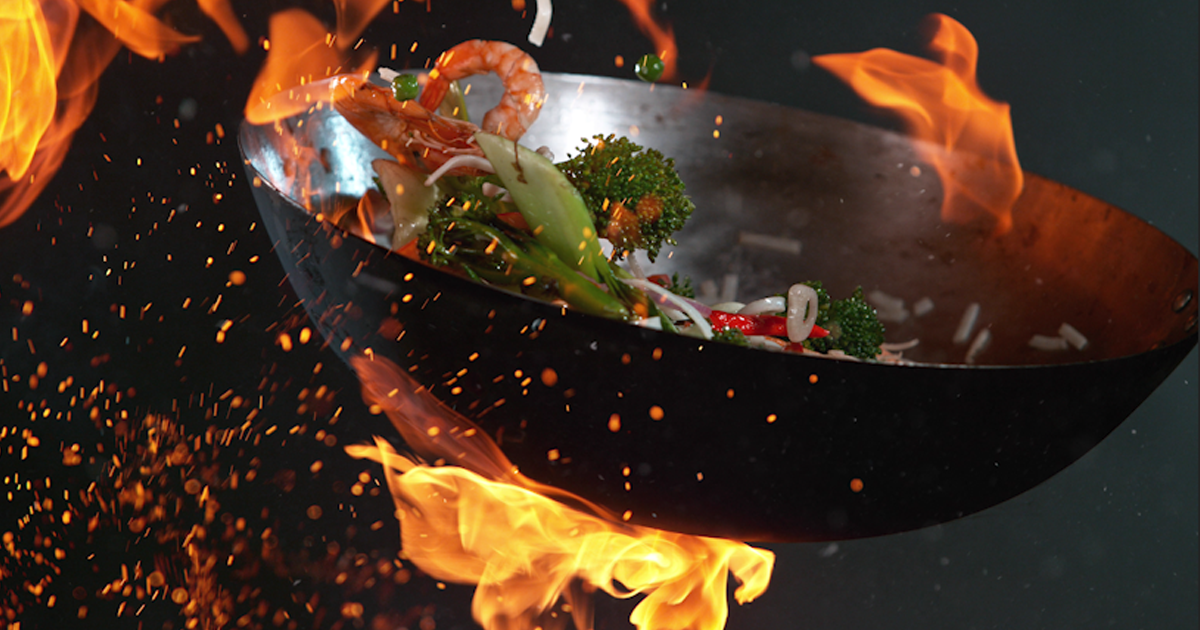 A wok tossing seafood and vegetables in over kitched flame
