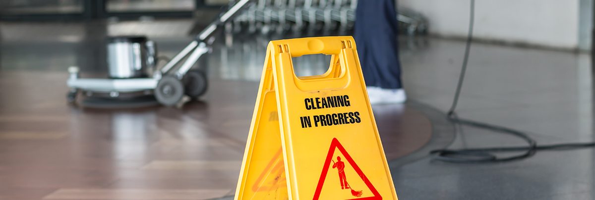 A janitor cleaning floor using a scrubber and a sign in front says cleaning in progress
